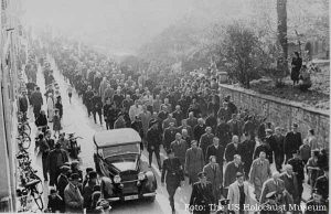 Homens judeus aprisionados na Noite dos Cristais marcham em Berlim, sob a guarda das SS, para assistir à destruição de uma sinagoga, antes de serem deportados. Os que ficaram serão posteriormente submetidos ao holocausto.